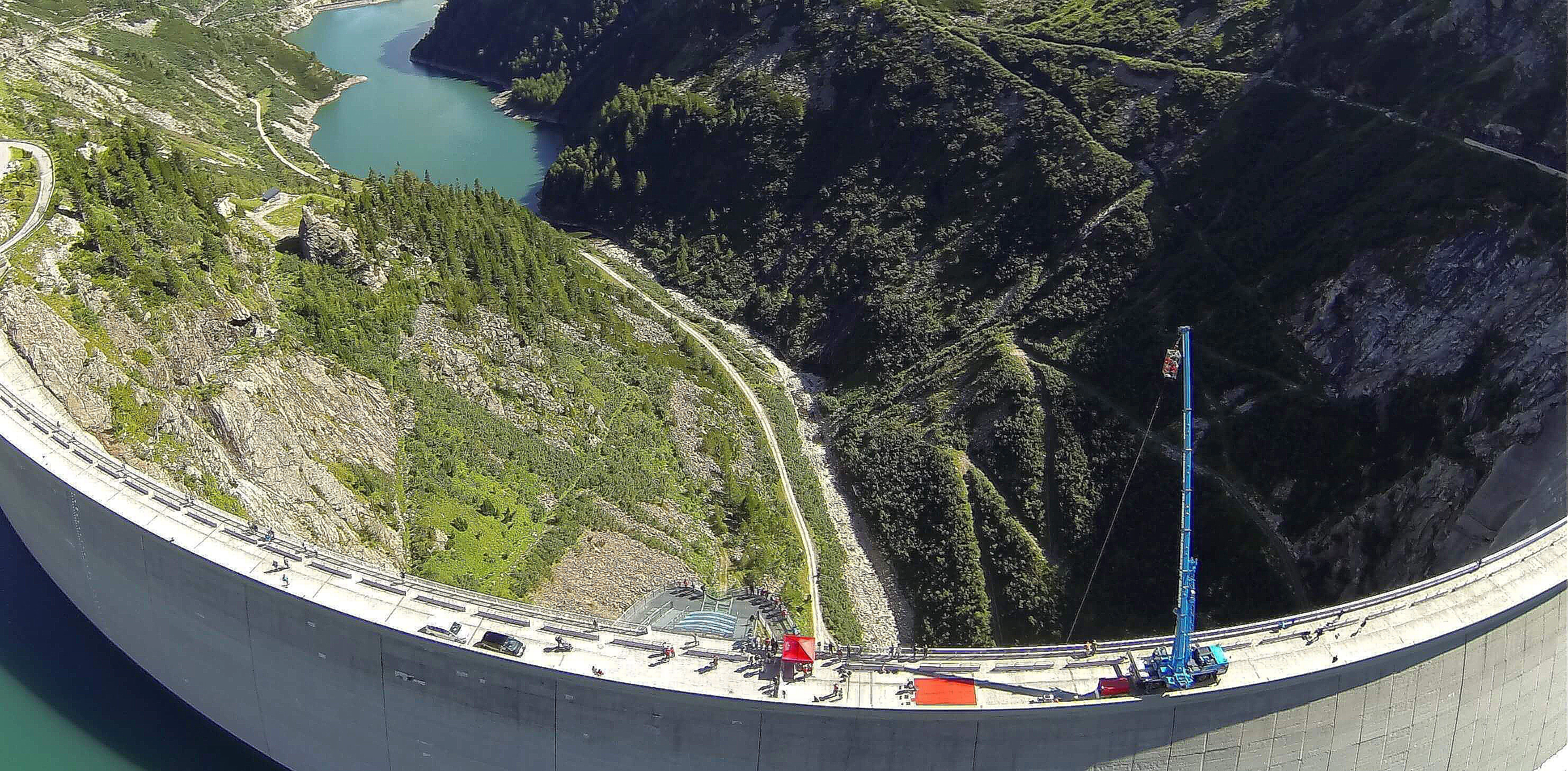 The aerial view shows the bungee jumping spectacle on the Malta Dam in summer. We see a large crane with a basket from which those interested can plunge into the depths.