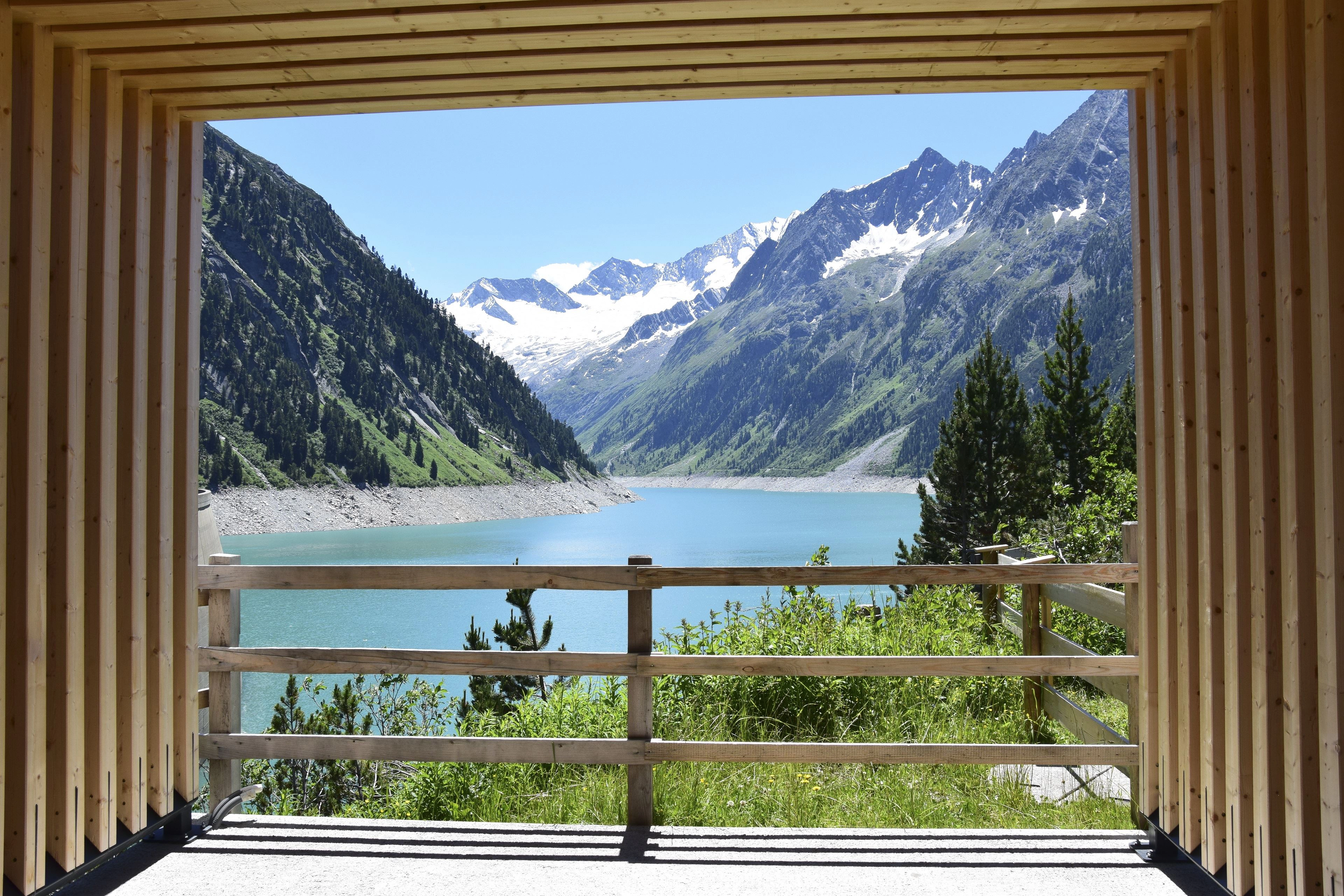 We look through a wooden construction onto the reservoir in Schlegeis. The water is a marvellous blue and the sun is shining. It's summer.