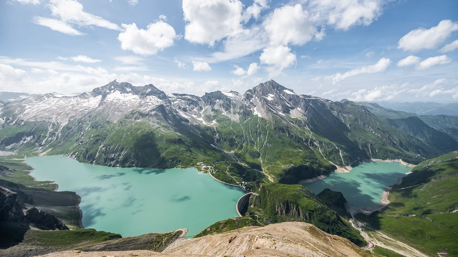 Wir blicken von einer erhöhten Perspektive auf die beiden Staussen in Kaprun. Der höher gelegene Mooserboden tront über den Wassfallboden. Im Wasser spiegeln sich die Schatten der Wolken.