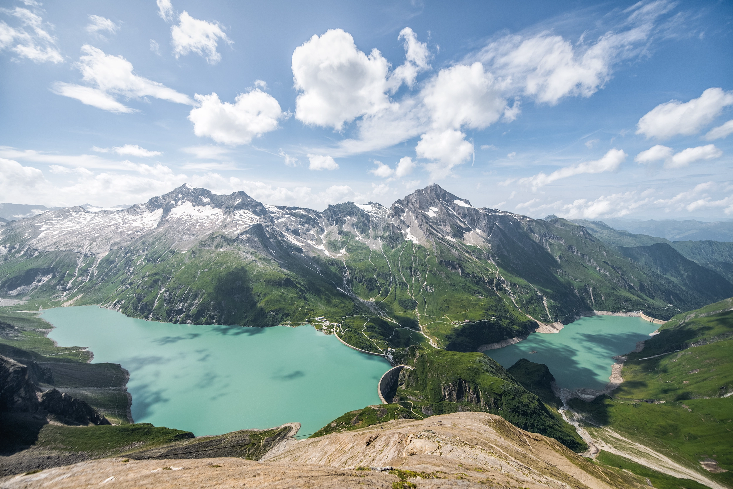 Wir blicken von einer erhöhten Perspektive auf die beiden Staussen in Kaprun. Der höher gelegene Mooserboden tront über den Wassfallboden. Im Wasser spiegeln sich die Schatten der Wolken.
