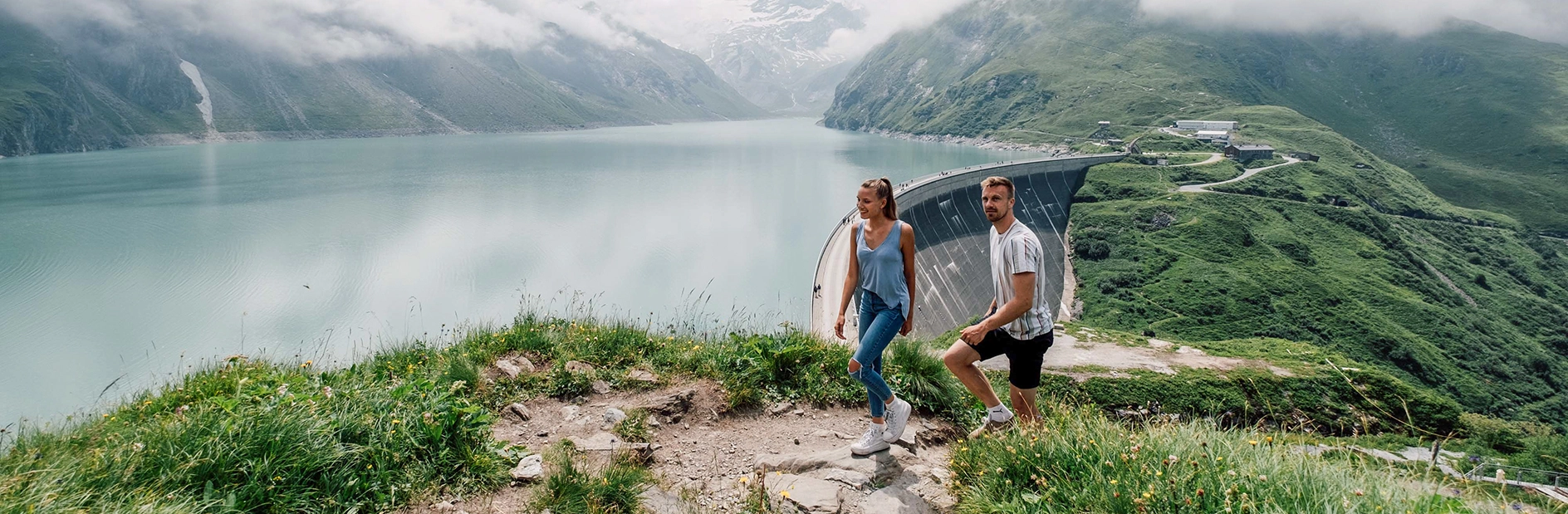 A young couple goes for a short hike on the Höhenburg in Kaprun. The sun is shining, but there are light wafts of mist over the Mooserboden.