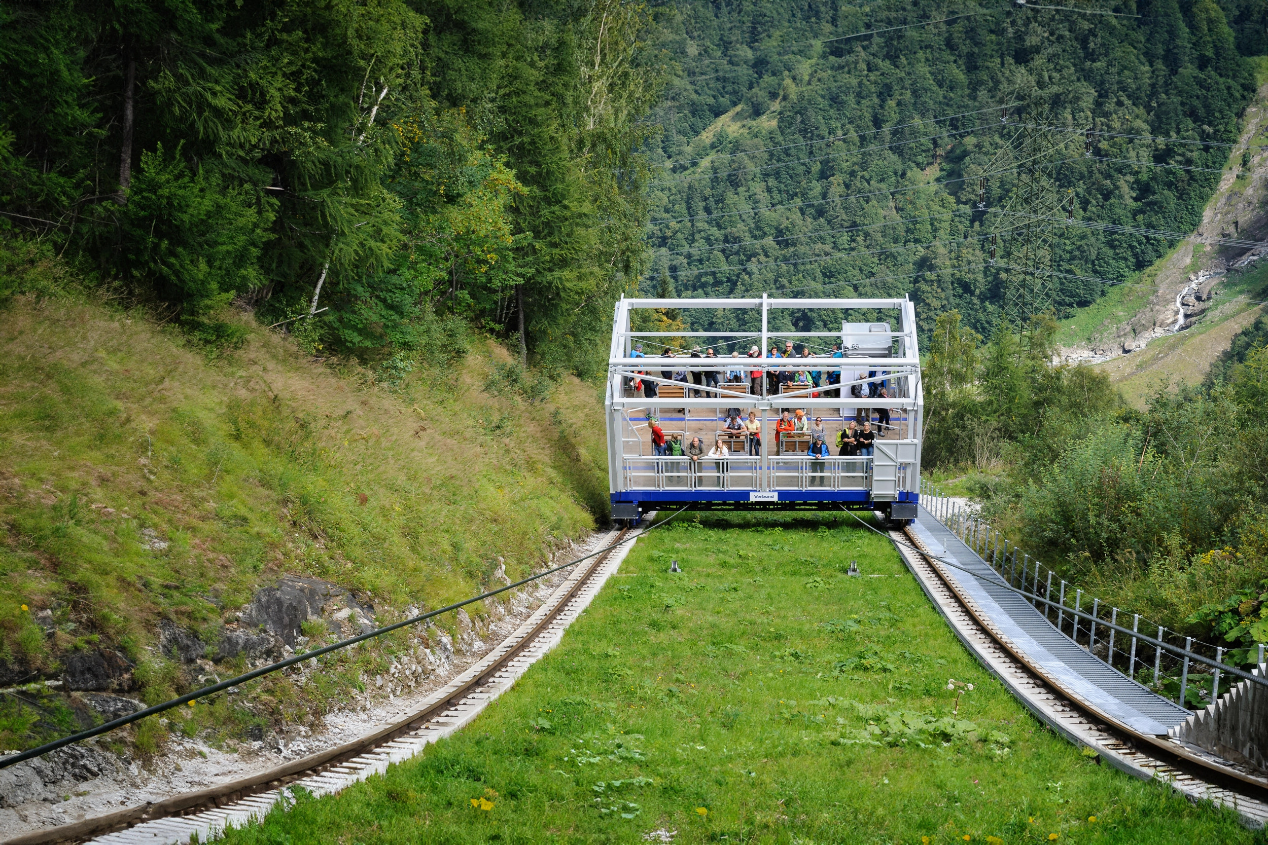 Ein Blick von oben auf den Lächwand Schrägaufzug in Kaprun. Die Wiesen sind saftig grün und die blau-weiße Metallkonstruktion bewegt sich mit einigen Besuchern in Richtung Ziel.