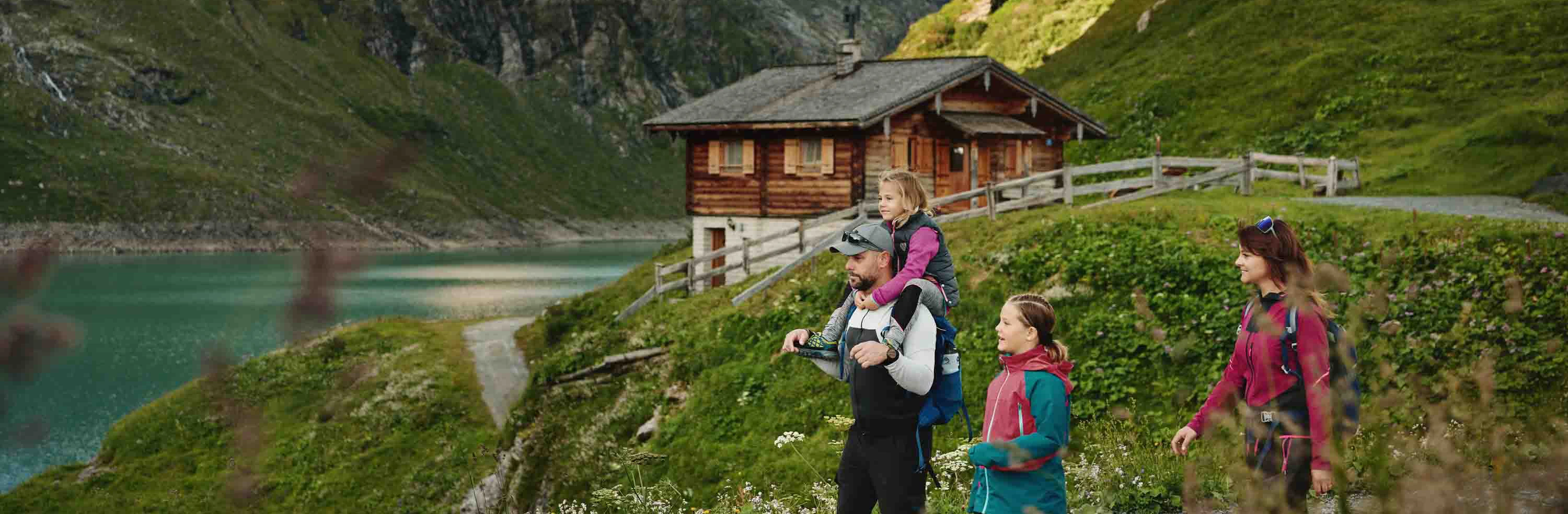 A family – consisting of a father, a mother and two children – are walking around the Mooserboden reservoir in weatherproof clothing.