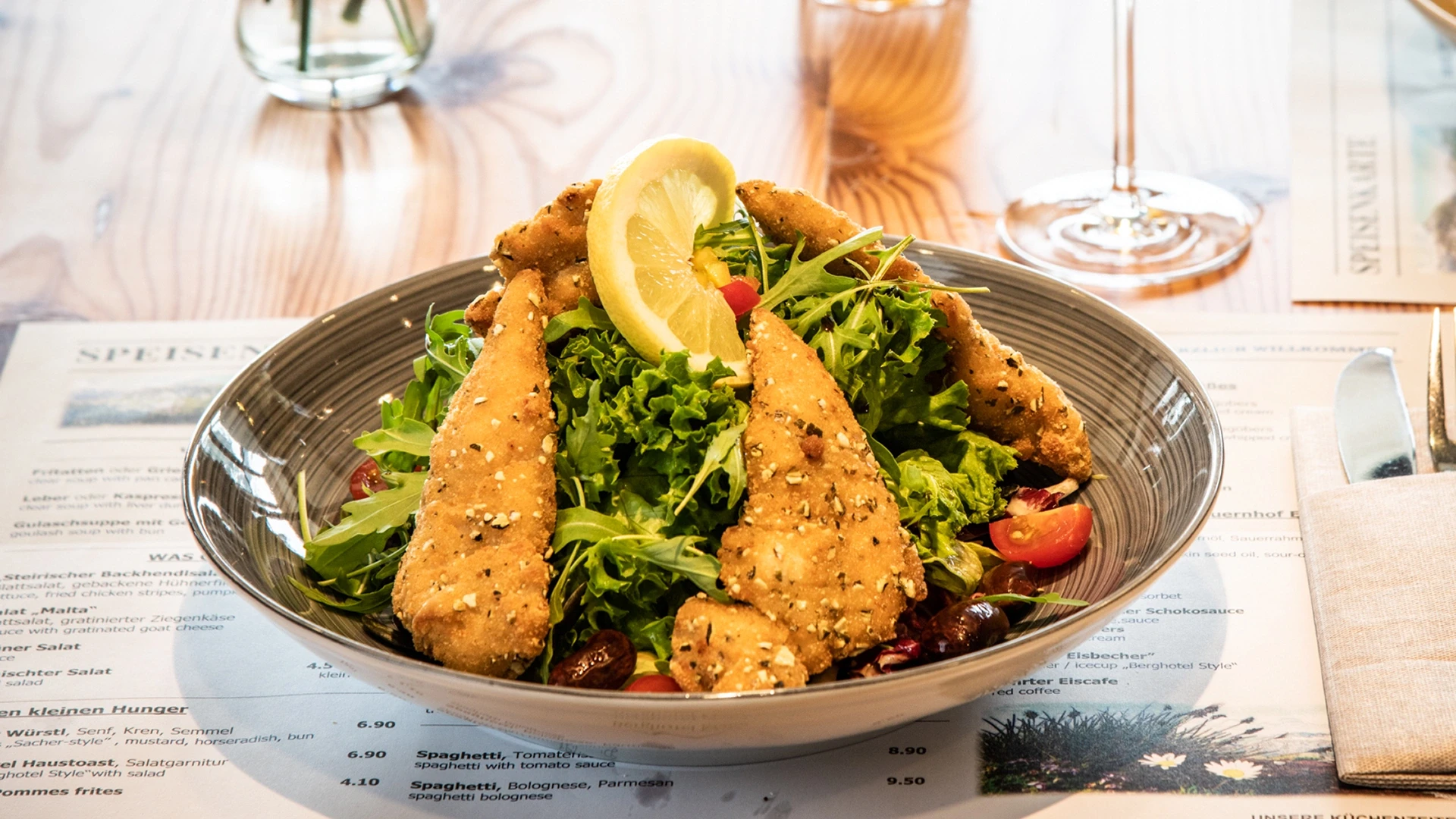 Ein brauner Bowl-Teller mit Backhendlsalat garniert mit einer Zitronenscheibe.
