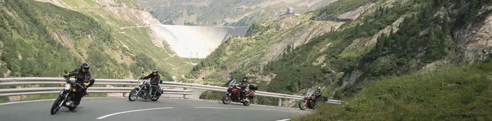 Wir sehen 4 Motorradfahrer auf der Zufahrtsstraße der Kölnbreinsperre. im Hintergrund sehen wir die Staumauer. Das Winter ist prächtig.