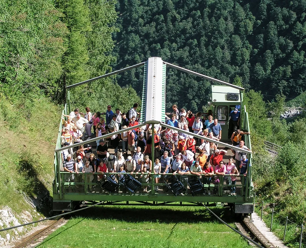 Wir sehen eine älter Farbaufnahme des Lärchwand Schrägaufzugs. In dieser Vorgängerversion besteht der Aufzug aus einer einfacheren offnen grünen Käfigkonstruktion. Zahlreiche Menschen fahren mit dem Aufzug gerade wieder nach unten. Wir blicken von oben auf die Passagiere.